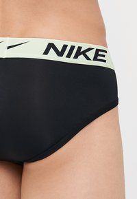 Sorte herreboxershorts med en lys grøn elastisk taljehynde, der har "NIKE" logoet i sort. Glat tekstur, tætsiddende pasform med buede sømme.
