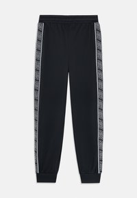 Juodos sportinės kelnės su elastinga juosmeniu ir manšetėmis, su balta Nike logotipo juosta, nusidriekiančia abiem išorinėm kelnėm.