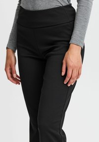 Black stretchy pants with a high waistband, smooth texture, and side seams. Paired with a long-sleeve gray top.