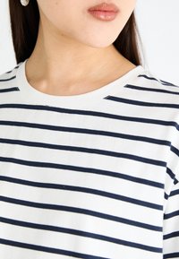 Cotton crew neck top featuring horizontal navy and white stripes, with a soft texture and relaxed fit. Notable details include a rounded neckline.