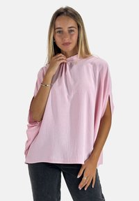 Rosa, strukturierter Pullover mit hohem Kragen, kurzen Ärmeln und Seitenschlitzen, kombiniert mit dunklen Denim-Jeans.