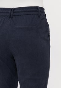 Marineblauwe corduroy broek met een gestructureerd oppervlak, voorzien van een tapered fit, elastische tailleband en twee achterzakken.