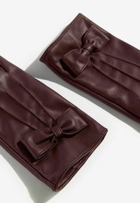 Burgundske usnjene rokavice z poudarjenim lokom, z nabranim dizajnom in gladko teksturo, ki prikazujejo prilegajočo in elegantno silhueto.