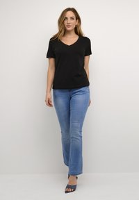 Melna V veida kakla T-krekla ar īsām piedurknēm, apvienota ar gaiši ziliem plats kāju džinsiem. Gluda auduma, ar pieguļošu siluetu; vienkāršs dizains.