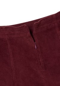 Gonna in corduroy bordeaux con texture a righe verticali, chiusura con zip sul retro e una vita con leggero dettaglio elastico.