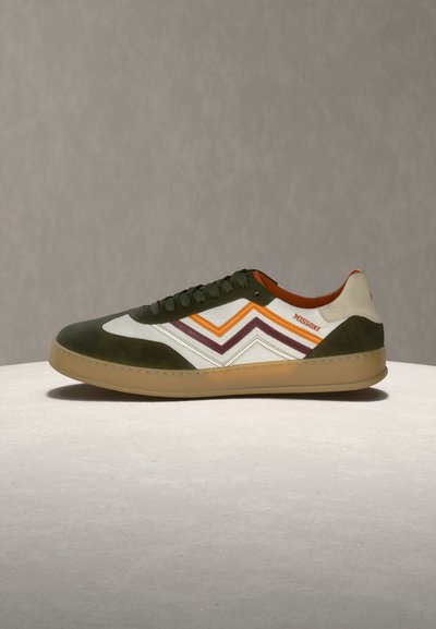 Baskets basses avec bout et talon en daim vert, côtés en cuir blanc ornés de bandes zigzag orange et violet, et semelle en caoutchouc beige.