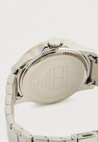 Stainless steel watch with a polished silver bracelet, textured gold accent on the bezel, and engraved details on the case back.