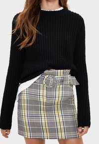 Černý pletený svetr s dlouhými rukávy, který je zkombinován s kostkovanou, vysokou mini sukni s žlutými, modrými a šedými vzory a páskem.