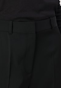 Pantalons noirs ajustés avec une texture lisse, dotés d'une passante de ceinture, d'une fermeture éclair et d'une taille structurée. Design simple avec des lignes épurées.
