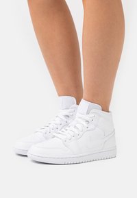 White high-top sneakers made of leather with a smooth texture, featuring lace-up design, padded collar, and subtle logo detail.