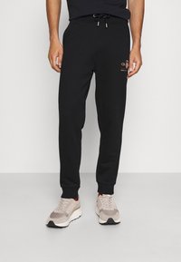 Zwarte sweatpants met een trekkoord in de taille en smal toelopende boorden. Bevat een klein gouden logo op de linker dij. Zacht, gemengd katoen materiaal.