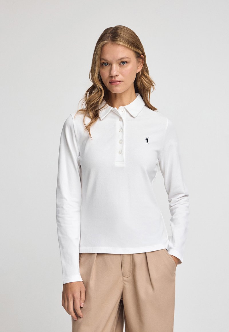 Vit långärmad polo t-shirt i bomull, med krage, knappstängning och en liten svart logotyp på vänster bröst.