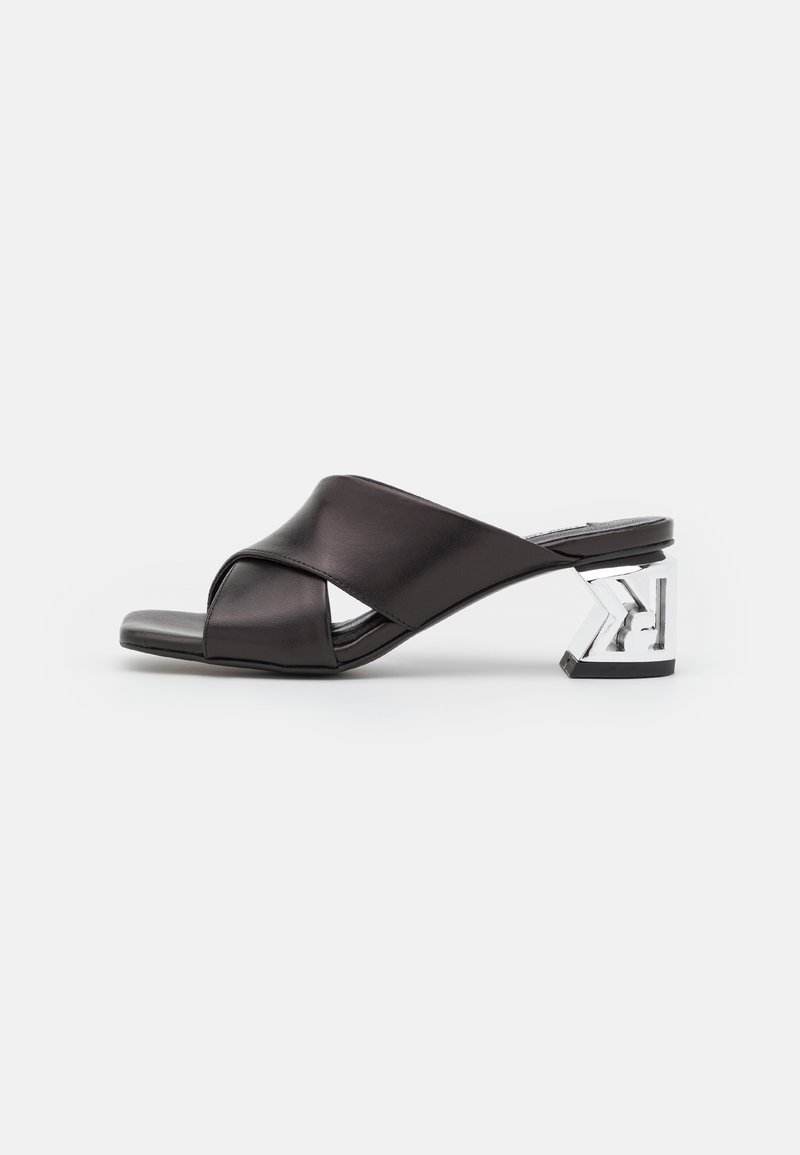 Sandale mule noire à bout ouvert avec larges brides croisées et talon bloc transparent avec un motif géométrique interne.