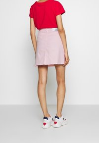 Vaaleanpunainen mini-hame, jossa on sileä rakenne ja takana tagi. Yhdistetty punaisen t-paidan ja sydänkoristeilla varustettujen valkoisten tennareiden kanssa.