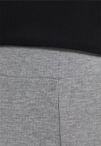 Šedé žebrované kalhoty z látky s měkkou texturou, s širokým elastickým pasem. Vrchní vrstva je jednobarevná černá a hladká.