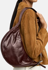 Brązowa skórzana torba hobo o luźnym kształcie, regulowanym pasku na ramię i gładkiej powierzchni. Minimalistyczny design z subtelnym połyskiem.