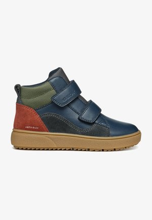 Zapatilla alta para niño en piel azul marino, malla verde, acentos de ante óxido, con doble cinta de Velcro y suela de goma texturizada.