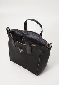 Borsa nera realizzata in materiale sintetico liscio con una cerniera dorata, dotata di manici doppi e un'accattivante accentatura con logo sul davanti. L'interno è grigio.