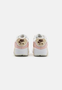 Nike Air tenisice s bijelim gornjim dijelom, ružičastim akcentima i bež petom. Imaju teksturiranu oznaku logotipa i udobnu potplat.