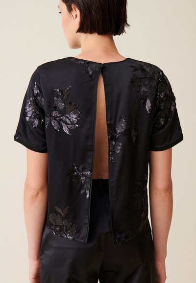 Top corto in satin nero a maniche corte con ricamo floreale in paillettes e schiena a chiave, che contrasta con il tessuto morbido per una maggiore varietà di texture.