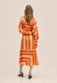 Vestido de manga larga en naranja y crema con llamativas rayas horizontales y verticales. Tejido suave con una textura lisa y corte a la altura de la rodilla.