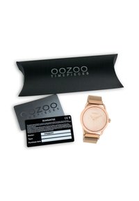 Montre-bracelet en maille rose doré avec un cadran crème texturé, accompagnée d'une boîte noire et d'une carte de garantie avec texte et logo blancs.