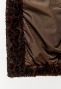 Nahaufnahme eines braunen Satin-Stoffs, der von einem dunkelbraunen und schwarzen Leopardenfellbesatz umrandet ist.