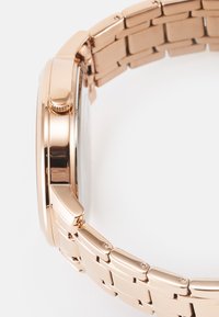 Montre-bracelet en or rose avec un cadran en métal poli et un bracelet à maillons. Elle possède un cadran rond, une couronne proéminente et une texture lisse.