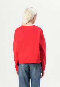 Sudadera roja con un corte relajado, cuello redondo y mangas largas. Acompañada de jeans de mezclilla azules con una textura ligeramente desgastada.