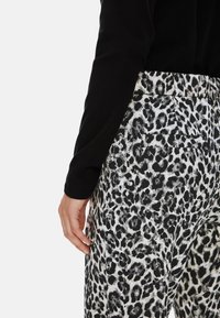 Leopardenmuster-Hosen in Schwarz und Weiß, aus strukturiertem Stoff. Mit einer Gesäßtasche und einem teilweise sichtbaren, schwarzen Langarmoberteil.