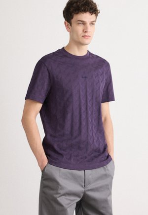 Violets īsām piedurknēm T-krekls ar teksturētu rakstu un apaļu kakla izgriezumu, kam pie krūšu ir neliels izšūts logotips.