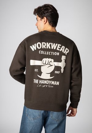 Braunes Sweatshirt mit einem großen weißen Grafikmotiv eines Hammers und Text auf der Rückseite. Gerippte Bündchen und Saum, lockere Passform, legeres Design.