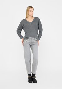 Maglione grigio lavorato a maglia con scollo a V, abbinato a jeans grigio chiaro decorati con elementi in cristallo sulle tasche. Stivaletti neri alla caviglia.