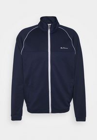 Navy zip-up jacket with white piping along seams, high collar, and two side pockets. Made from soft, textured fabric. Logo on chest.