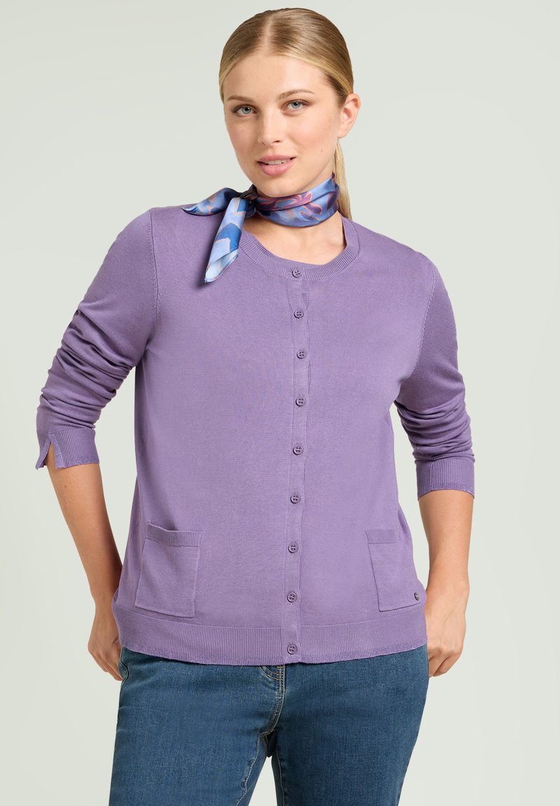 Fioletowy sweter z dzianiny z okrągłym dekoltem, z guzikami z przodu i dwoma kieszeniami. Posiada długie rękawy z podwiniętymi mankietami. Gładka faktura.