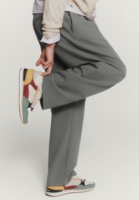 Ljust grå, plisserade byxor kombinerade med flerfärgade sneakers med röda, gula, blå och gröna detaljer. Gummisula, strukturerad tyg.