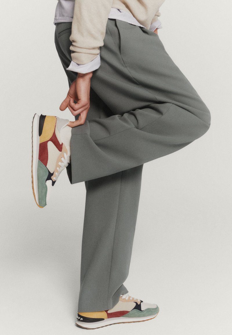 Ljust grå, plisserade byxor kombinerade med flerfärgade sneakers med röda, gula, blå och gröna detaljer. Gummisula, strukturerad tyg.