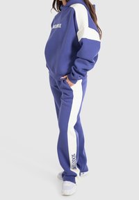 Purple hoodie and matching joggers with white side stripes. Hoodie features logo on the chest, both in a soft, textured fabric.