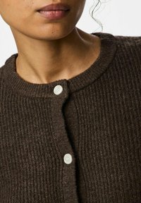 Cardigan de canalé marrón oscuro fabricado en un material texturizado, con un escote redondo y un cierre de un solo botón blanco.