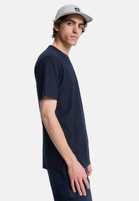 Navy blue cotton t-shirt with short sleeves and a crew neckline, paired with dark pants and a light gray cap featuring ventilation holes.