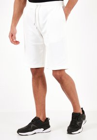Hvide atletiske shorts i en bomuldsblanding med elastisk talje og snøre, der har en afslappet pasform og sidelommer. Kombinationen er med sorte sneakers.