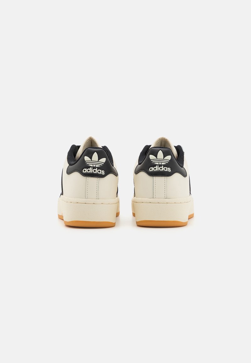 Beżowe i granatowe niskoprofilowe sneakersy z skórzaną cholewką, gumową podeszwą i teksturowanymi akcentami. Zawierają biały detal logo na pięcie.
