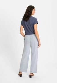 Marineblauw T-shirt met korte mouwen, gedragen met brede gestreepte broeken. De outfit heeft een relaxte pasvorm en twee achterzakken, aangevuld met bruine blokhak sandalen.