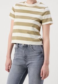 Camiseta cropped a rayas en verde oliva y crema, con un cuello redondo. Combinada con unos jeans de mezclilla gris de corte slim.