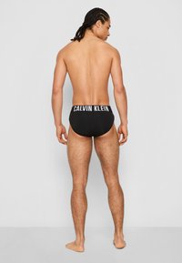 Zwarte boxershorts met een witte "CALVIN KLEIN" logo op de elastische tailleband, ontworpen met een strakke pasvorm en minimale bedekking achter.