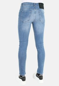 Blauwe skinny jeans van denim met een gladde textuur, vijf zakken ontwerp en een zwarte leren achterpatch. Draagt met witte en zwarte sneakers.