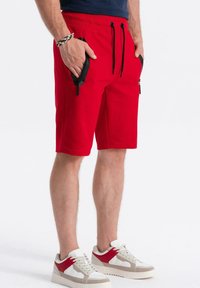 Rode sportieve shorts met een koord in de taille, met zwarte ritszakken en een zachte, gestructureerde stof. Gemaakt in combinatie met witte en rode sneakers.