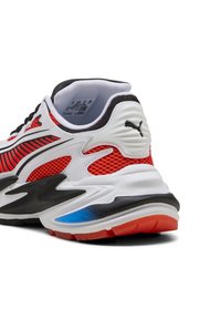 Parte trasera de una zapatilla Puma roja, blanca y negra con paneles de malla, suela gruesa y con la marca en el talón y el lateral.