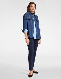 Jeansowa kurtka z ćwiekami, zestawiona z jasnoniebieską koszulą, granatowymi spodniami slim-fit i ciemnobrązowymi balerinami. Gładki materiał i dopasowany krój.