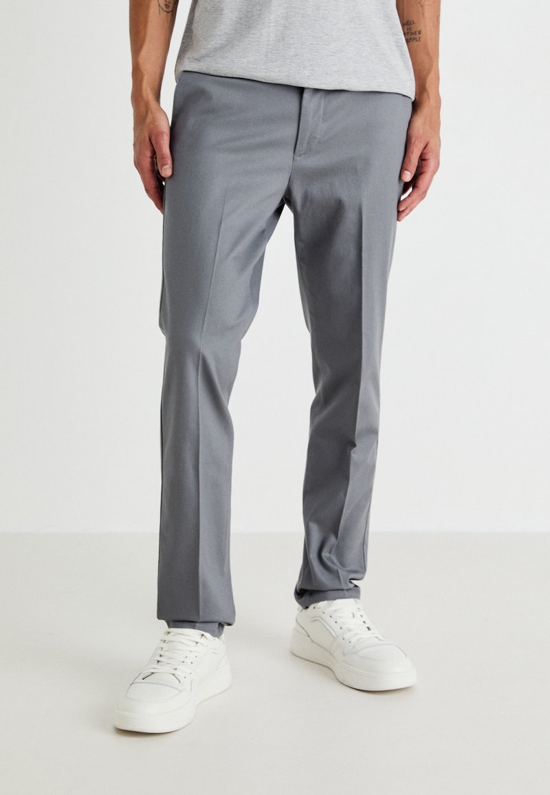 Grå skreddersydde bukser laget av glatt stoff, med slim fit, sidelommer, og kombinert med hvite sneakers for kontrast.